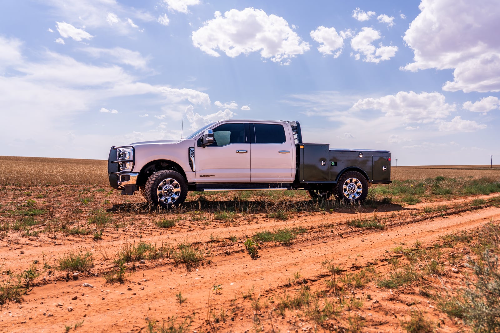 Side profile of a black Apollo service body on a white pickup beneath a bright field sky.