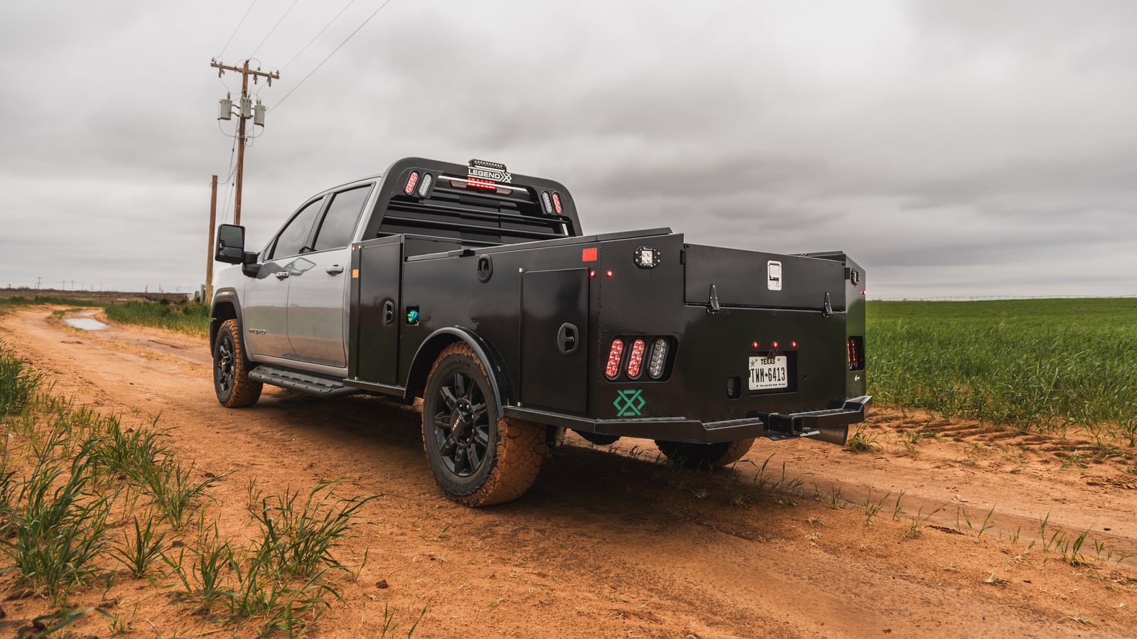 Black Legend X Apollo service body on a gray pickup parked on a dirt road beside a green field.