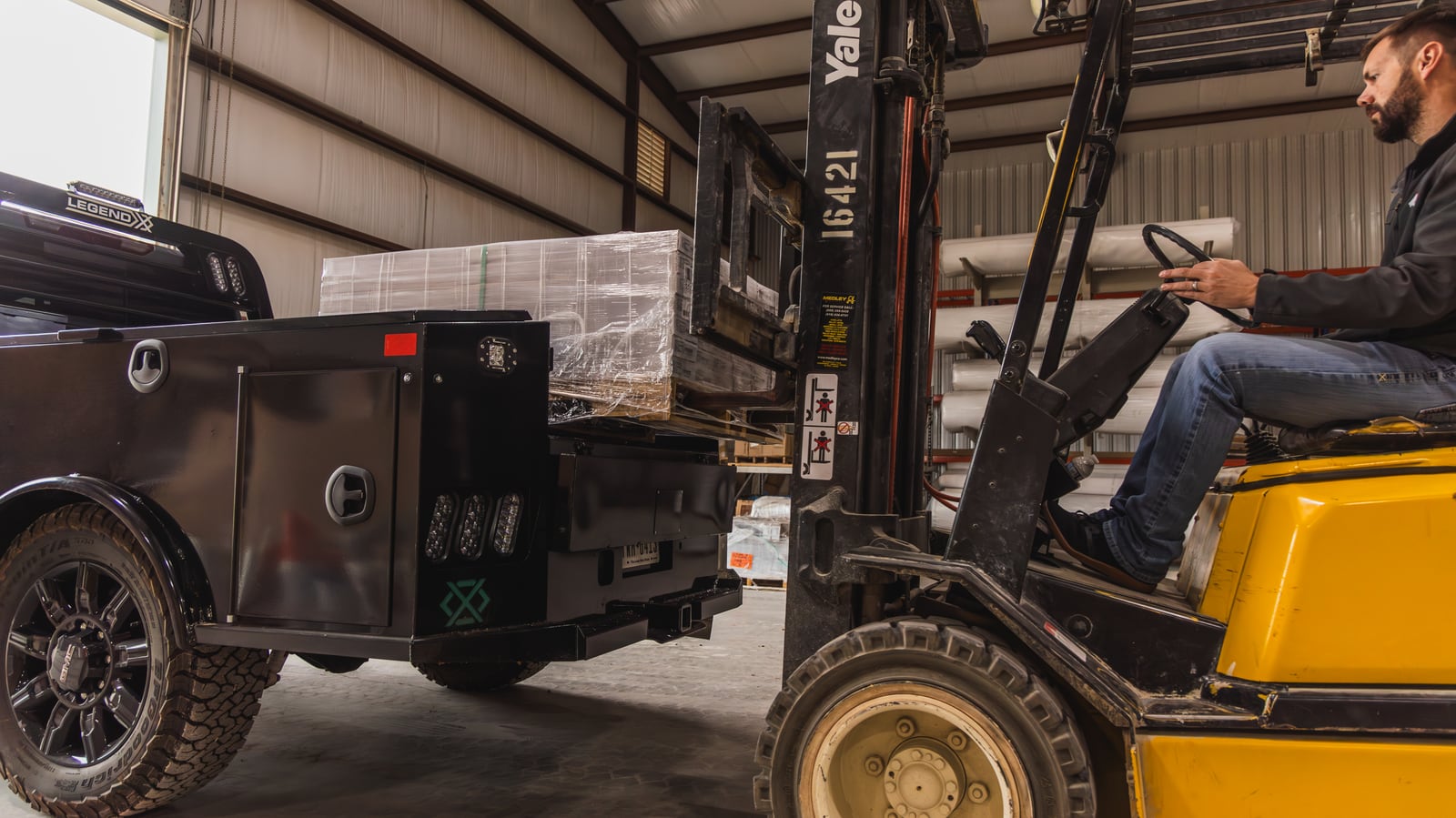 Forklift operator loading a pallet onto a black Legend X Apollo service body.
