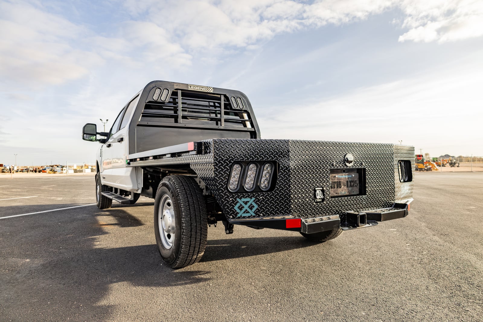 Low rear view of a black Legend X Spartan flatbed showing the diamond-plate skirt, lights, and hitch.