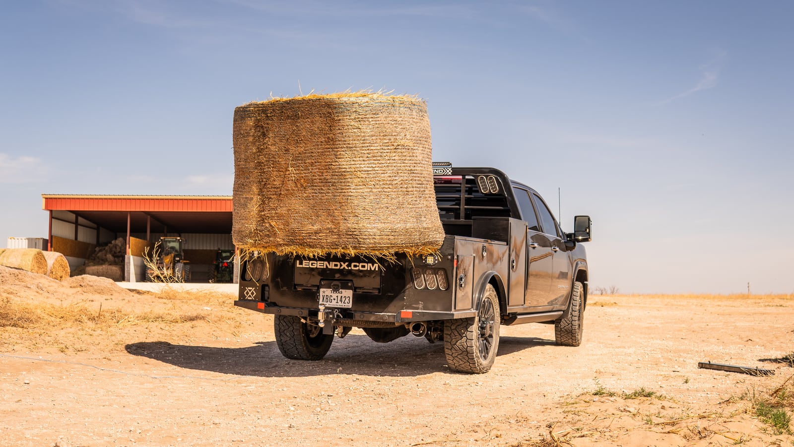 Black Legend X bed lifting a round hay bale on a gray pickup at a ranch.
