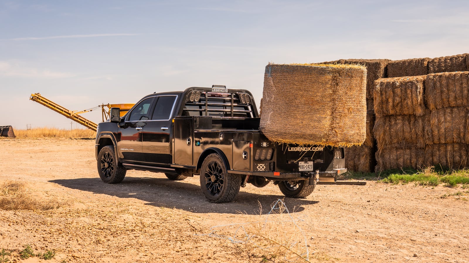 Black Legend X spike bed carrying a large hay bale beside stacked bales.