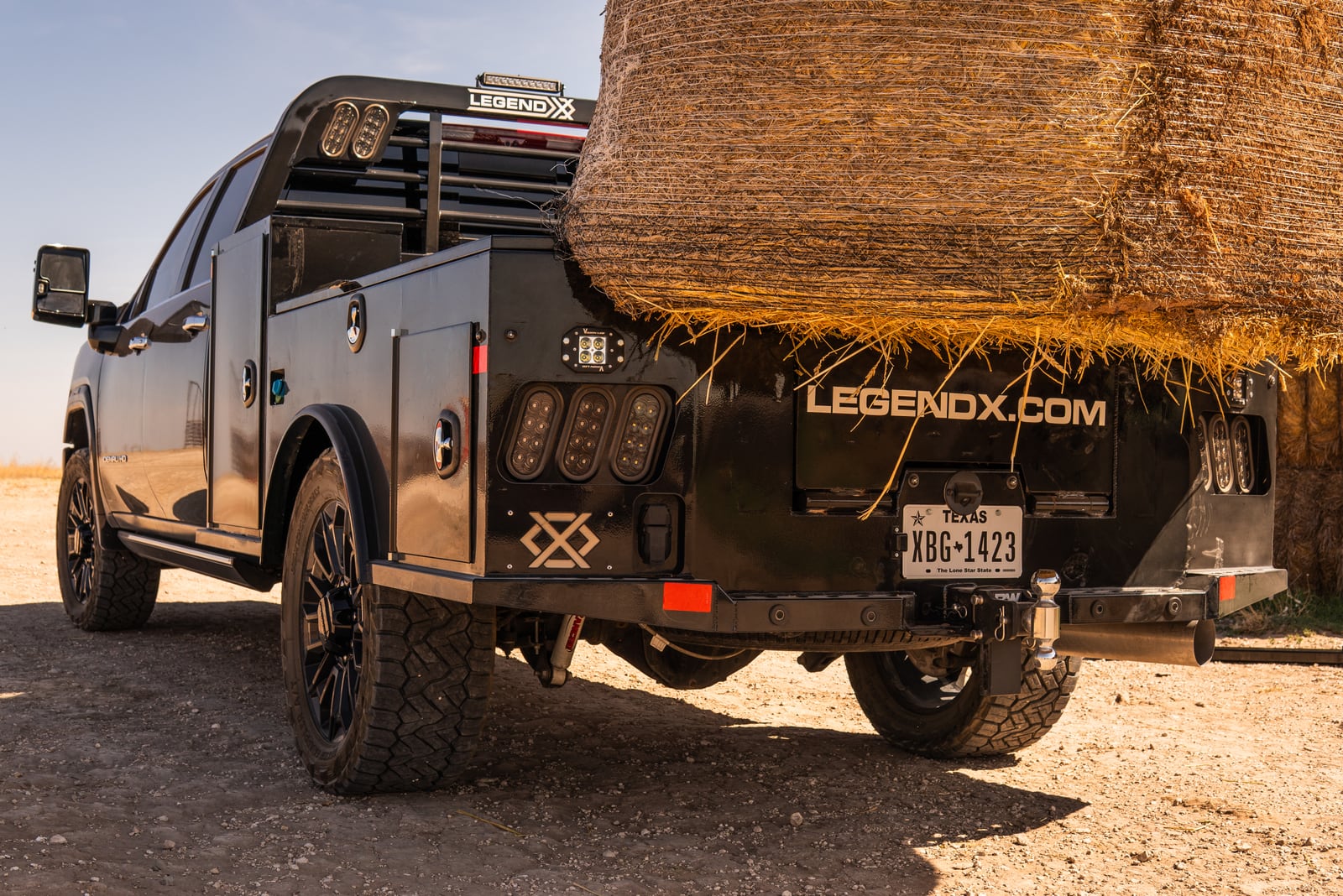 Rear three-quarter view of a black Legend X bed carrying a round hay bale.