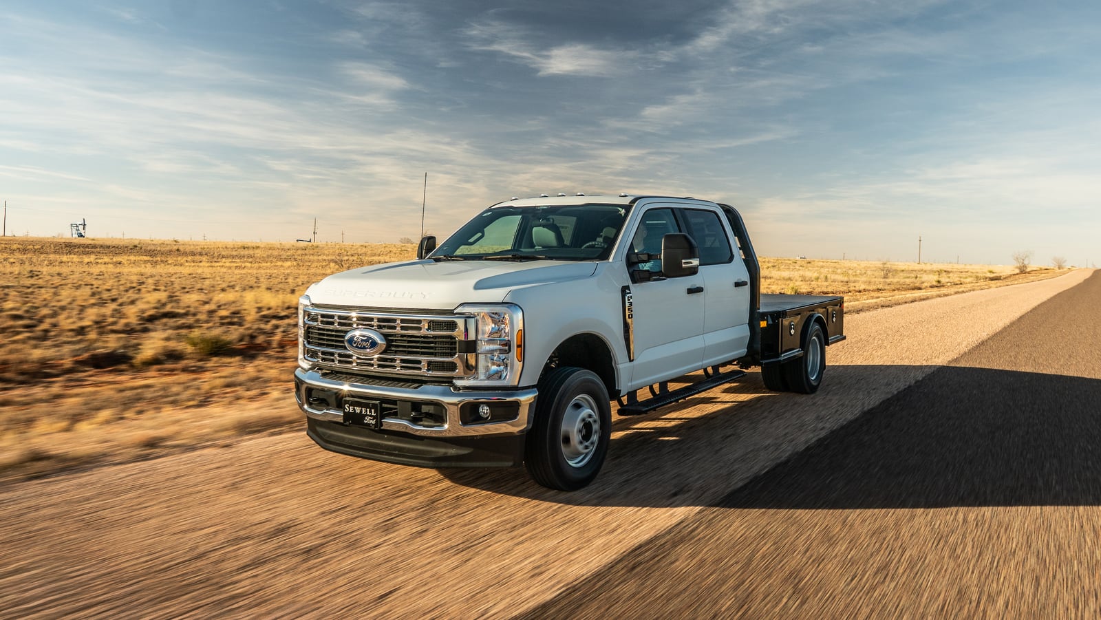 White pickup with a black Legend X Viking flatbed driving on a rural road.