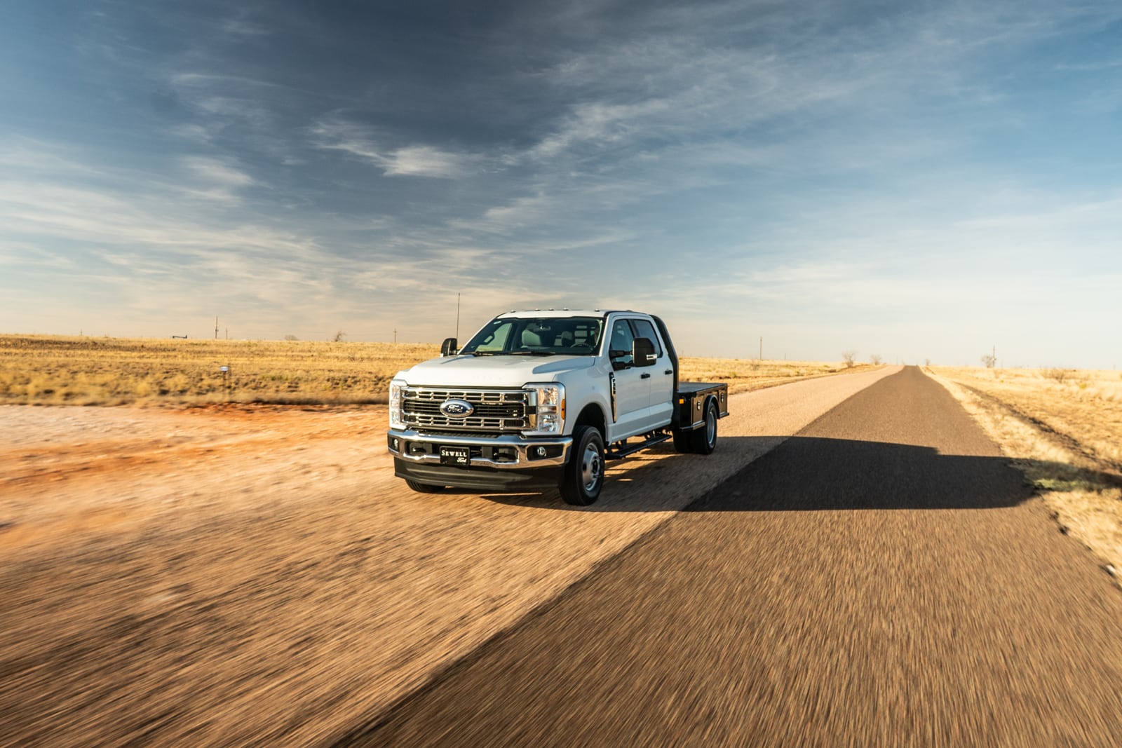 White Ford work truck with a black Legend X Viking flatbed driving on an open rural road.